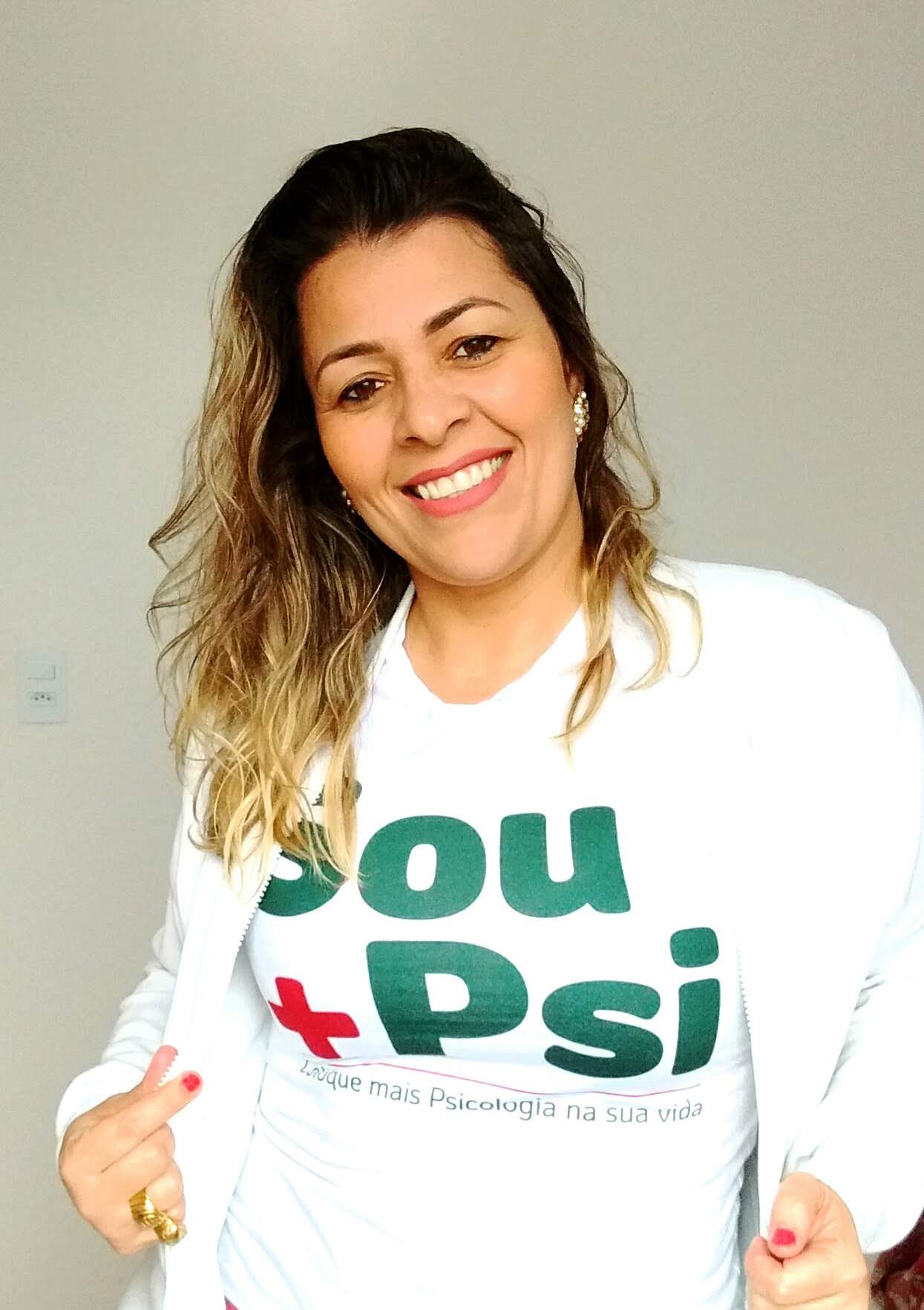 Mulher morena, cabelos escuros com mechas loiras, vestindo camiseta escrita Sou +PSI e sorrindo